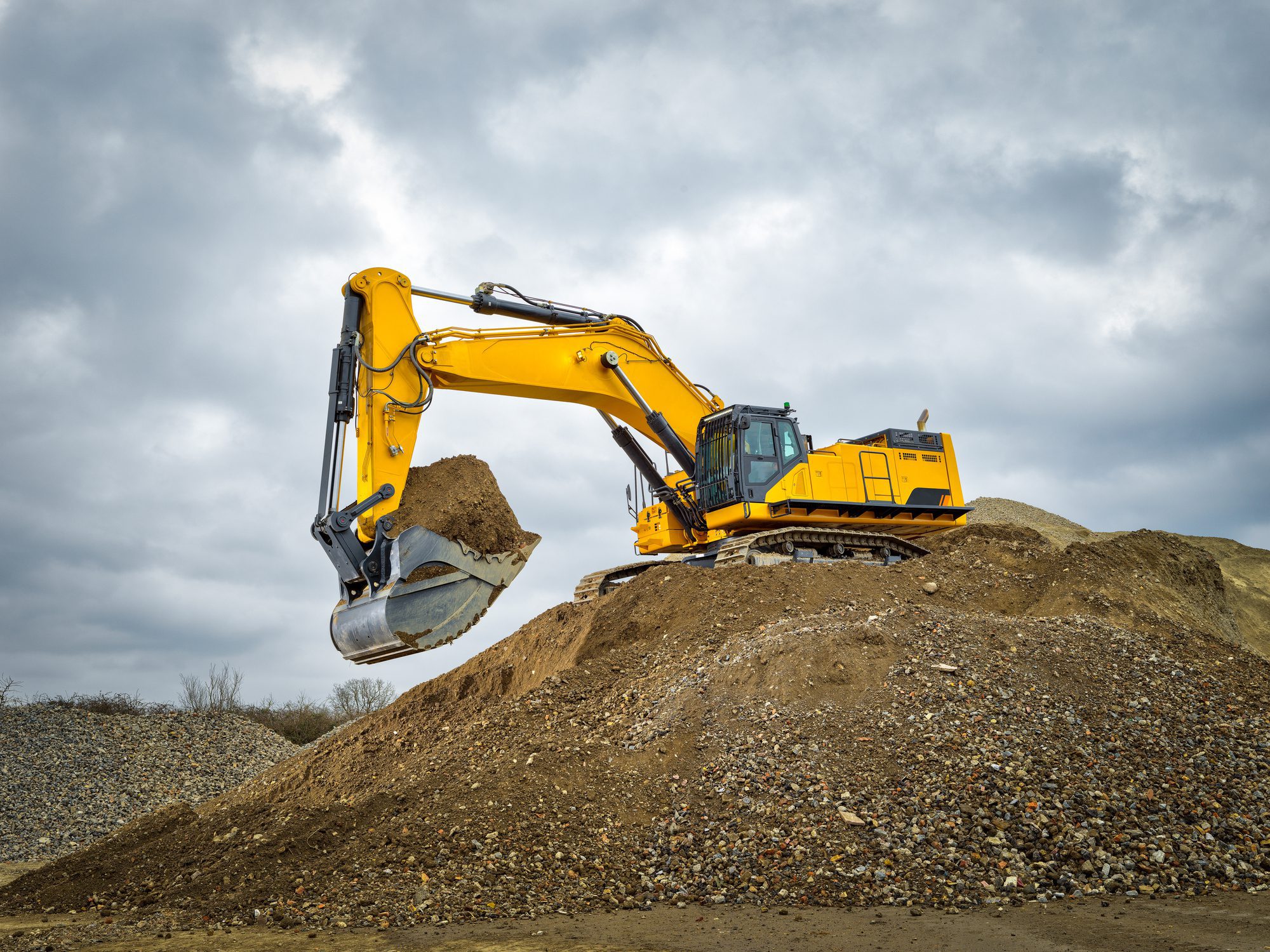 Yellow excavator scooping dirt on gravel mound